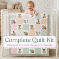 Meadow Fawn baby quilt kit – finished quilt with watercolor deer, florals and sage and blush patchwork, held by a smiling baby
